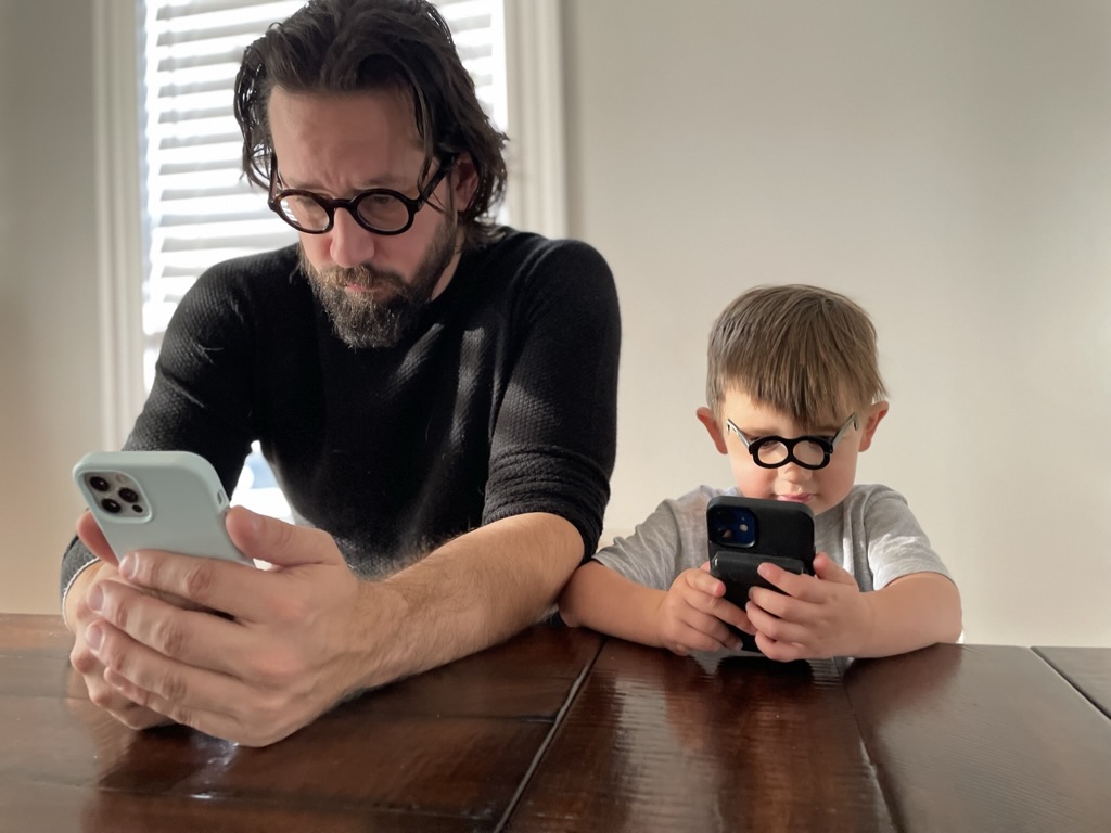 Nick and his son Teddy, both holding iPhones in front of them, Teddy wearing glasses to emulate Nick