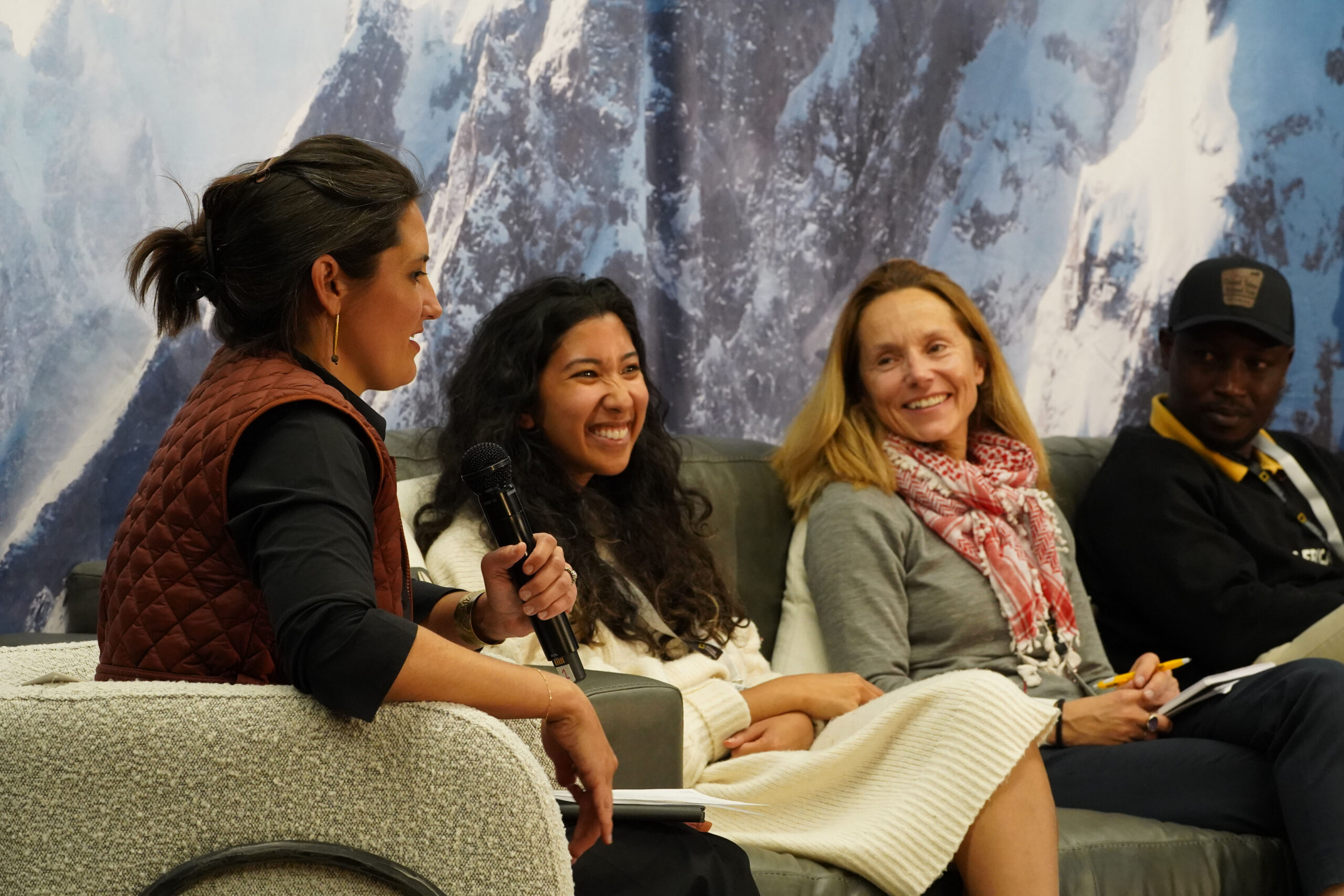 Katie and three other people sit on a panel in front of a mountain backdrop, smiling and talking during a discussion.