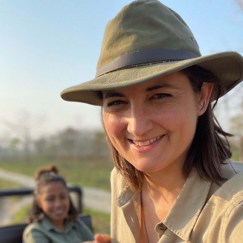 Katie wearing a khaki shirt and green hat in an open jeep with another person blurred in the background.