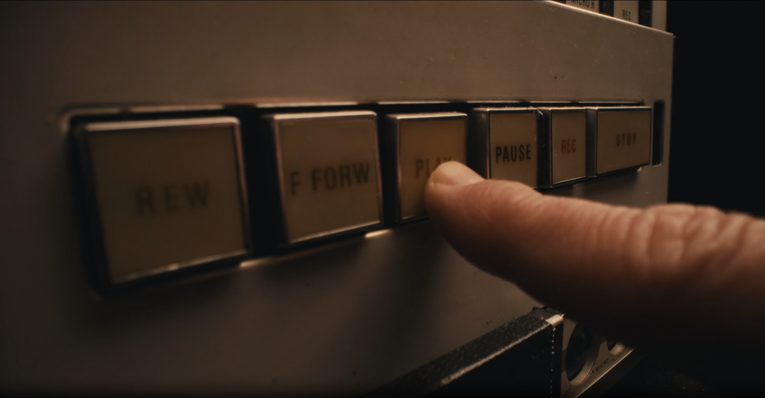 A close-up of a finger pressing the “Play” button on an old audio recorder with labeled control buttons.